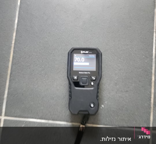 מד לחות על רצפה אפורה, קשור לאיתור נזילות.